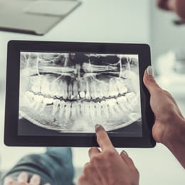 Dentist reviewing panoramic dental X-ray on tablet with patient during consultation.