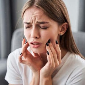 Woman experiencing tooth pain, holding her cheek with both hands indoors.