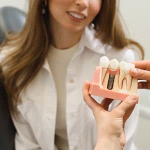Woman in white coat holding dental implant model in clinical office setting.