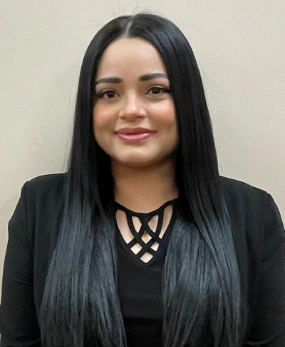 Professional headshot of woman with long dark hair wearing black blazer in dental office setting.