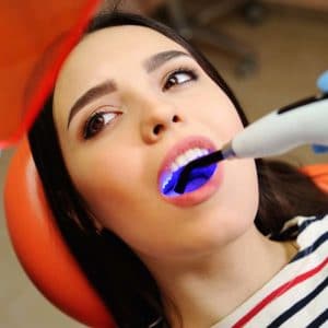 Woman receiving professional teeth whitening treatment with blue LED light at dental clinic.