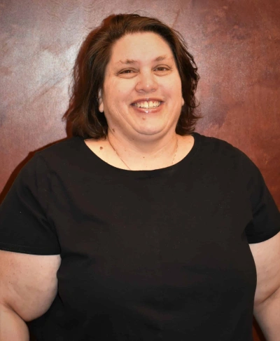 Professional headshot of smiling woman in black shirt against brown studio background.