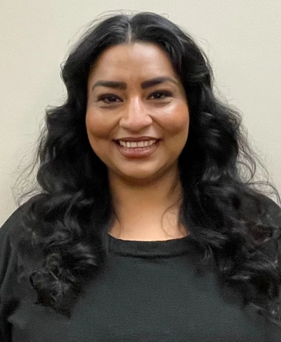 Smiling woman with long black hair wearing dark shirt in professional dental office setting.