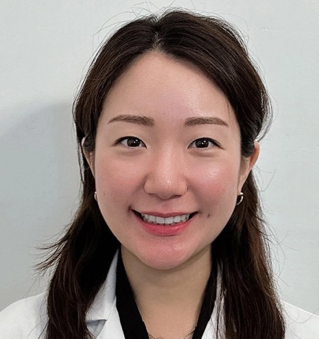 Professional headshot of smiling female dental staff member wearing white coat against neutral background.