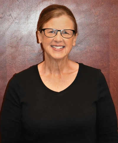 Woman wearing glasses and black shirt smiling at camera against pink textured background portrait