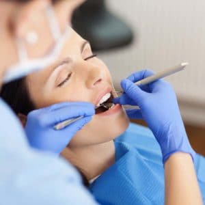 Patient receiving dental examination in dental office with dentist wearing blue gloves.