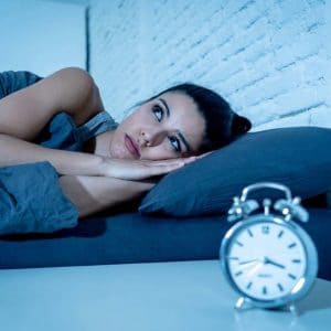 Woman lying awake in bed at night with alarm clock, depicting insomnia or sleep problems.