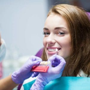 Young woman smiling while holding dental model in dental office wearing purple gloves