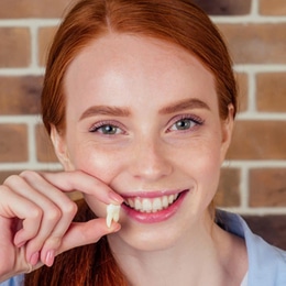 Young woman with red hair smiling brightly against brick wall background at dental office.