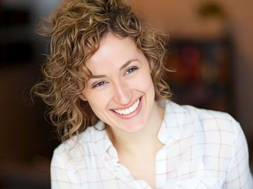 Smiling woman with curly hair wearing white shirt in dental office setting.