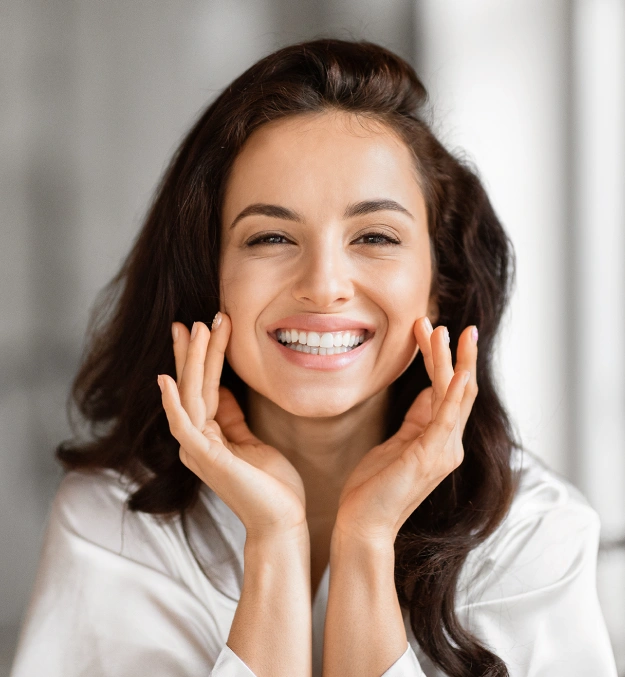 Smiling woman with dark hair touching her face in bright dental office setting.
