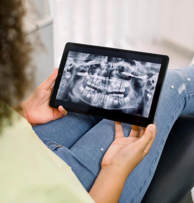 Person holding tablet displaying dental X-ray in clinical setting.