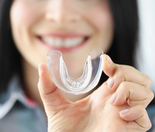 Woman smiling while holding clear dental aligner tray in front of her face