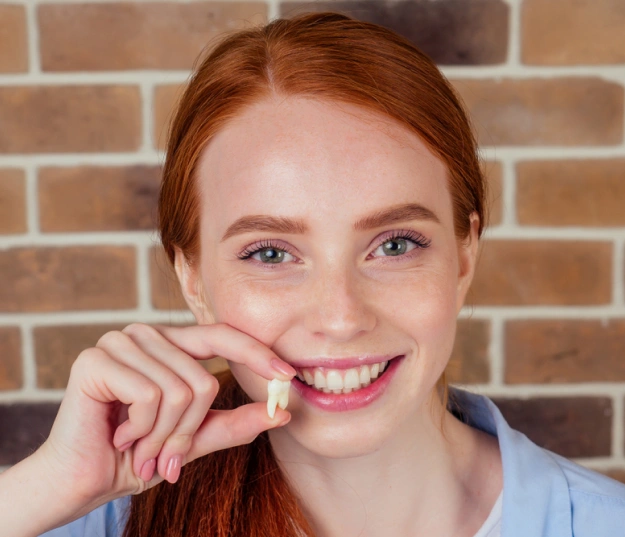 Smiling woman with red hair holding dental floss against brick wall background