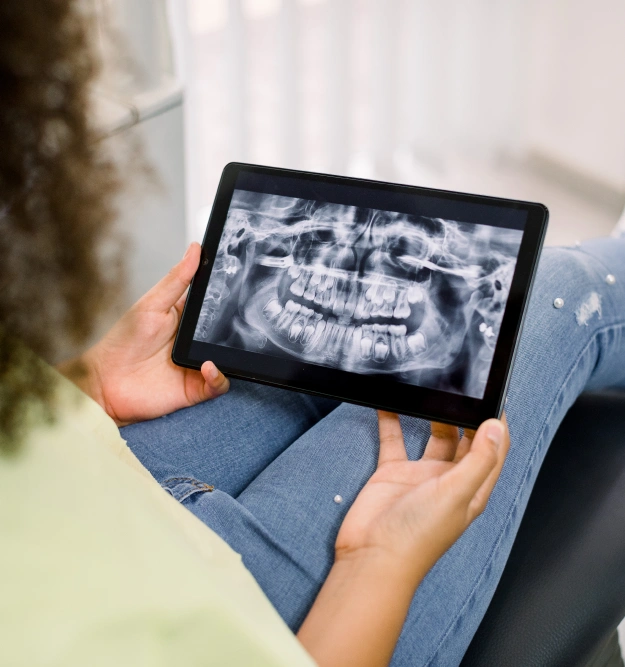 Person holding tablet displaying dental X-ray scan in clinical setting.