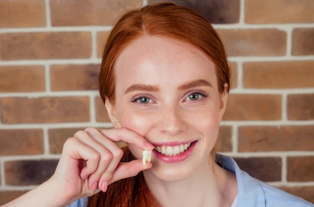 Smiling woman with red hair against brick wall, hand near face, dental office portrait.