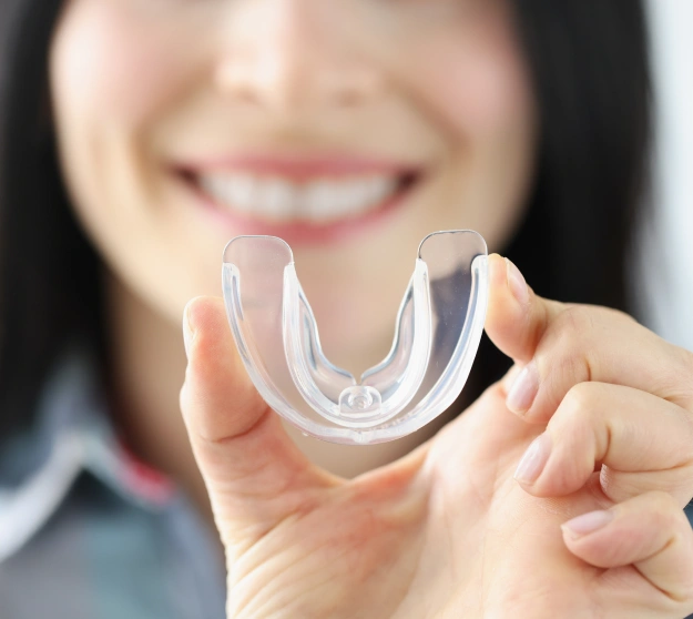 Woman holding clear dental retainer, smiling in background at dental office
