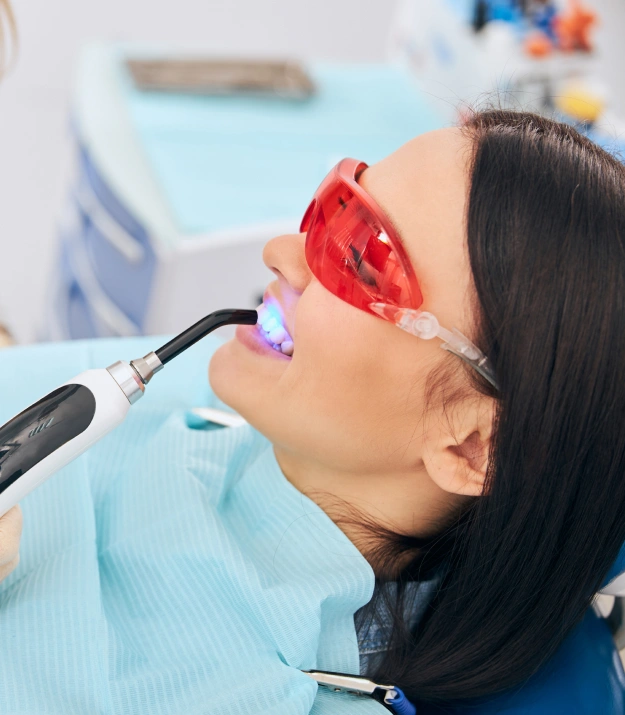 Patient receiving dental treatment with red protective eyewear in modern dental office.
