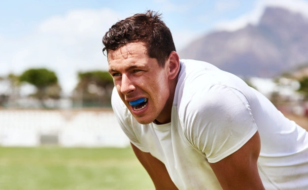 Man in white shirt stretches outdoors on sunny day with mountains in background.